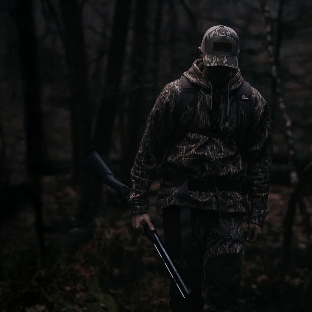 Guy walking through woods with gun