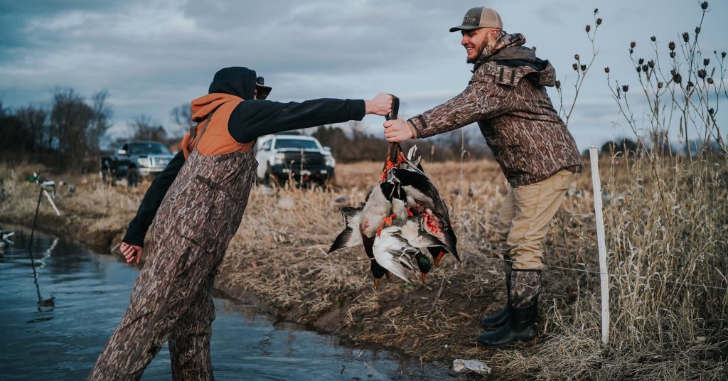 man passing ducks to another man
